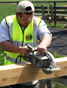 A Greencorps Chicago trainee sawing lumber to build a raised planting bed.